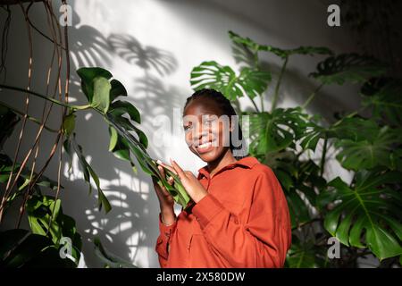 Porträt, fröhliche afroamerikanerin im urbanen Dschungel. Pflanzen Sie Liebhaber Mädchen im sonnigen Gewächshaus Stockfoto