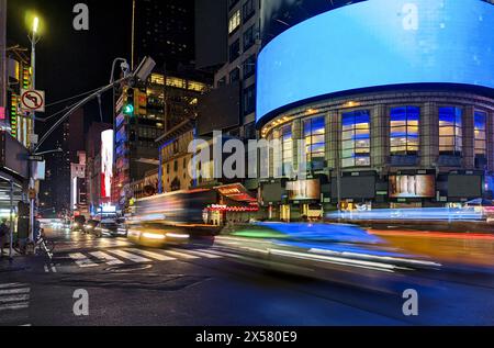 Eine geschäftige Kreuzung mit Autos, Bussen und Taxis, die nachts auf der 42nd Street durch den Times Square in New York City fahren Stockfoto