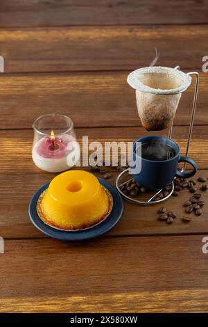 Kleiner Quindim, traditionelles brasilianisches Süßes, neben einer Tasse Kaffee und einer Kerze 2. Stockfoto