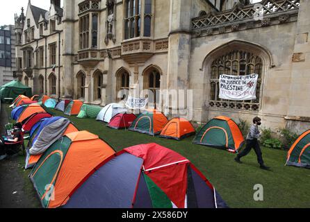 Ein Demonstrant schreitet zwischen den Zelten, während ein Banner vor dem Kings College über dem Kings College mit der Aufschrift „Cambridge Jews for Justice in Palestine“ fliegt. Vor dem King's College in Cambridge wurde ein Protestlager zur Unterstützung Palästinas eingerichtet. Die Besatzungsmitglieder des Lagers rufen die Universität auf, eine ethische Prüfung durchzuführen, alle Investitionen einzustellen, Stiftungen Forschungskooperationen mit allen Organisationen, die an der israelischen Besetzung Palästinas und dem Völkermord in Gaza mitschuldig sind, werden zu einer Uni of Sanctuary für palästinensische Flüchtlinge und unterstützen palästinensische Studenten und Akademiker. Protest Stockfoto