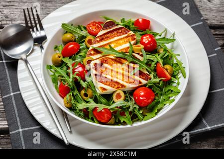 Gesunder Salat mit gegrilltem griechischen halloumi-Käse, Rucola, Tomaten und grünen Oliven in weißer Schüssel, Blick auf die Landschaft, Nahaufnahme Stockfoto