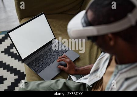 Hochwinkelansicht eines nicht erkennbaren Schwarzen Mannes, der ein VR-Headset mit Laptop trägt, Kopierraum Stockfoto