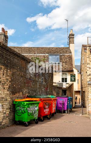 Farbenfrohe Abfalleimer, die an einer Ziegelmauer entlang Miltons Walk zur Cut Throat Alley mit Graffiti angereiht sind. Cambridge, England, Großbritannien Stockfoto