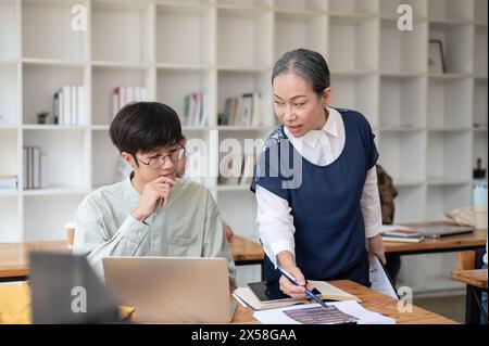 Eine reife asiatische Lehrerin, die ihrer Schülerin in der Klasse hilft und schwierige mathematische Probleme erklärt. Bildungskonzept Stockfoto