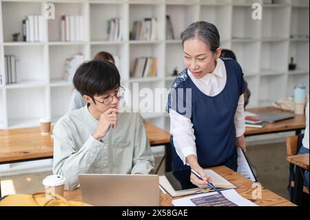 Eine reife asiatische Lehrerin, die ihrer Schülerin in der Klasse hilft und schwierige mathematische Probleme erklärt. Bildungskonzept Stockfoto