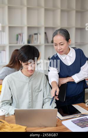 Eine reife asiatische Lehrerin, die ihrer Schülerin in der Klasse hilft und schwierige mathematische Probleme erklärt. Bildungskonzept Stockfoto