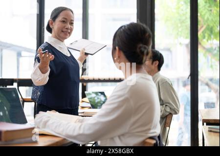 Eine reife asiatische Lehrerin, die ihrer Schülerin in der Klasse hilft und schwierige mathematische Probleme erklärt. Bildungskonzept Stockfoto