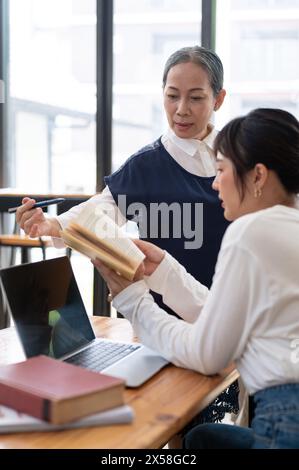 Leitende asiatische Lehrerin, die ihrer Schülerin in der Klasse schwierige mathematische Probleme erklärt. Bildungskonzept Stockfoto
