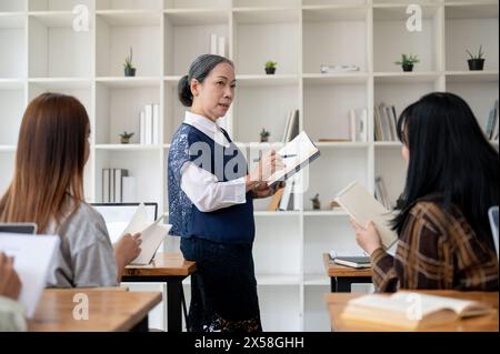 Eine professionelle, reife asiatische Lehrerin oder Professorin unterrichtet im Klassenzimmer, hält ihren Schülern einen Vortrag, erklärt eine Lektion oder diskutiert Stockfoto