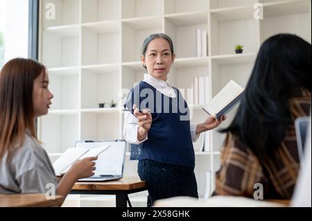 Eine professionelle, reife asiatische Lehrerin oder Professorin unterrichtet im Klassenzimmer, hält ihren Schülern einen Vortrag, erklärt eine Lektion oder diskutiert Stockfoto