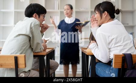 Zwei junge asiatische Studenten flüstern, reden gern und ignorieren die Lektion im Klassenzimmer. Tratsch, Universitätsleben, Bildung Stockfoto