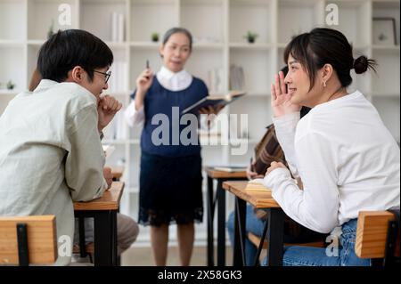 Zwei junge asiatische Studenten flüstern, reden gern und ignorieren die Lektion im Klassenzimmer. Tratsch, Universitätsleben, Bildung Stockfoto