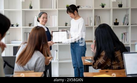 Eine reife asiatische Lehrerin oder Professorin, die einem Schüler im Klassenzimmer einen Preis oder ein Zertifikat verleiht. Bildungskonzept Stockfoto