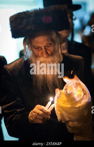 Ein bärtiger, älterer jüdischer Mann, der einen Streimelhut trägt, zündet ein Lagerfeuer während einer traditionellen lag B'Omer-Feier in Jerusalem, Israel. Stockfoto