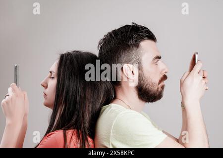 Trotz körperlicher Nähe konzentrieren sich ein Mann und eine Frau ausschließlich auf ihre Smartphones, was das Paradoxon von Verbindung und Isolation im digitalen Zeitalter symbolisiert Stockfoto