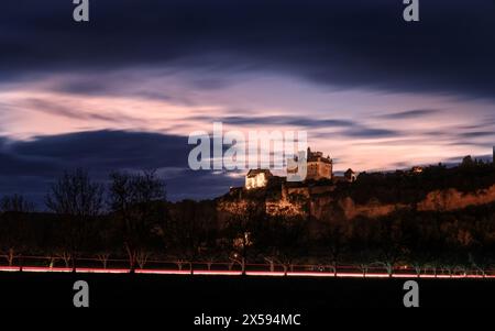 Beynac-et-Cazenac, Frankreich - 6. Mai 2024: Sonnenuntergang über dem Chateau de Beynac in der französischen Dordogne mit leichten Spuren von Autos im Vordergrund Stockfoto