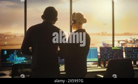 Weibliche und männliche Fluglotsen mit Headsets sprechen im Airport Tower. Büroraum voller Desktop-Computer-Displays mit Navigationsbildschirmen, Flugradardaten für Steuerungen. Stockfoto