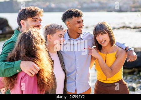 Eine lebhafte Gruppe von verschiedenen Freunden lacht zusammen während eines entspannten Ausflugs am Meer und zeigt echtes Glück und starke Bande in einer natürlichen Umgebung Stockfoto