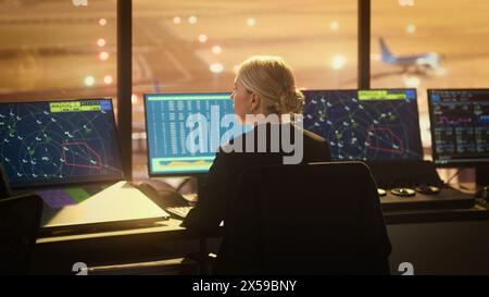 Porträt einer Fluglottin, die im Flughafenturm arbeitet. Der Büroraum ist voll von Desktop-Computer-Displays mit Navigationsbildschirmen, Flugradardaten. Stockfoto