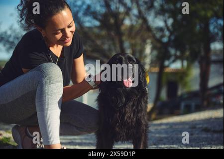 Junge hübsche Frau, die Spaß hat, Zeit mit ihrem Haustier im Freien zu verbringen, mit ihrem verspielten Cocker Spaniel Hund auf der Natur zu gehen. Haustiere spielen, Haustierkonzept. Stockfoto