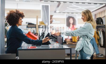 Kassenschalter für Bekleidungsgeschäft: Verkaufsleiter für Frauen und Männer akzeptieren NFC-Smartphone-Zahlungen von einem jungen, stilvollen weiblichen Kunden für neue, stilvolle Kleidung. Stockfoto