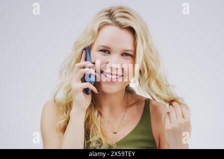 Porträt, Frau und Sprechen auf dem Smartphone im Studio mit Fingern im Haar zum Flirten, Happy oder Chat auf weißem Hintergrund. Lässige Mode, Lächeln und Stockfoto