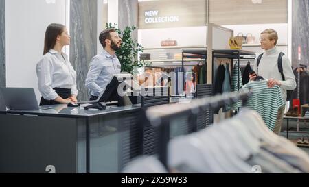 Bekleidungsgeschäft: Gutaussehender junger Mann an der Kasse kauft Kleidung von einem freundlichen Vertriebsassistenten. Einkaufszentrum mit Designermarke. Trendiges Modegeschäft mit Designer-Marken. Stockfoto