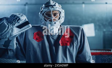 Eishockey Rink Arena: Porträt des brutalen Profi-Torhüters, der Torhüter-Maske trägt und die Kamera ernsthaft betrachtet. Fokussierter Torwart, entschlossen zu gewinnen. Souveräner Champion Athlet. Nahaufnahme Stockfoto