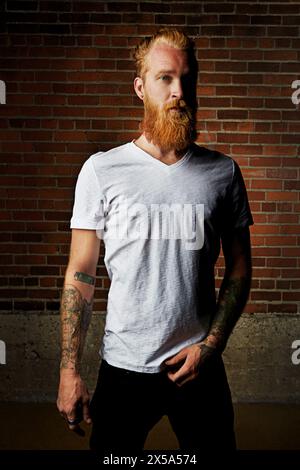 Mann, Porträt und selbstbewusste Kleidung von Ziegelwänden, Stolz und Tätowierung oder Hemd im Freien. Männliche Person, ernstes Gesicht und Gen z oder lässiges Outfit für Stockfoto