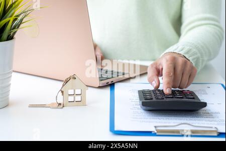 Makler oder Makler, der mit Immobiliendokumenten arbeitet und Hypothekenkosten mit dem Rechner berechnet. Aufwendungen für die Refinanzierung des Wohnungsdarlehens Stockfoto