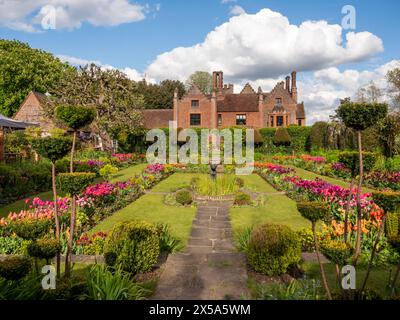 Chenies Manor House und Gärten auf dem Höhepunkt der Tulpensaison. Blauer Himmel und Wolken über dem Herrenhaus Tudor mit Blick auf den gepflegten versunkenen Garten. Stockfoto