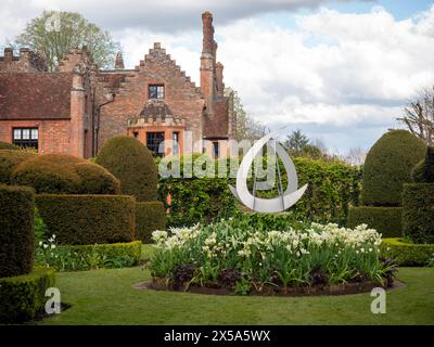 Chenies Manor House aus dem Topiary Garden mit Skulpturen und weißen Tulpen in einem runden Blumenbeet. Stockfoto