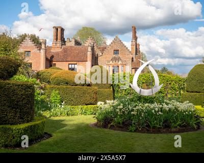 Chenies Manor House aus dem Topiary Garden mit Skulpturen und weißen Tulpen in einem runden Blumenbeet. Stockfoto