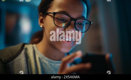 Porträt eines Jugendlichen multiethnischen Schwarzen Mädchens mit Smartphone. Junge Frauen durchsucht das Internet, sucht soziale Medien, chats mit Freunden. Sie trägt Brillen und Zahnspangen. Stockfoto