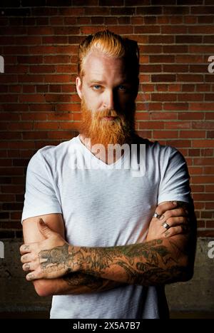 Mann, Porträt und selbstbewusstes Outfit mit Ziegelwänden, Stolz und Ringen oder Schmuck für Tattoo-Stil. Männliche Person, ernsthaftes Gesicht und Gen z oder Arme überkreuzt Stockfoto