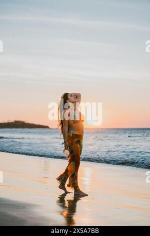 Eine Frau genießt einen ruhigen Spaziergang entlang der Küste von Costa Rica bei Sonnenuntergang, während die untergehende Sonne einen warmen Glanz über den Sandstrand wirft und sanft W Stockfoto