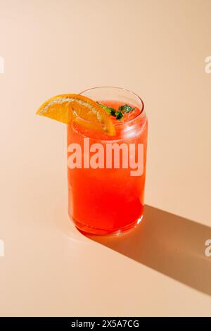 Ein lebendiges Glas Beeren-Orange-Limonade garniert mit einer frischen Orangenscheibe und Minze, kalt mit Eis auf einem neutralen Hintergrund serviert. Stockfoto