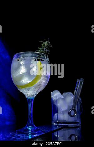Klassischer Gin Tonic Cocktail in einem Ballonglas mit Eis und einer Scheibe Limette, Zange und Eiswürfeln, die an der Seite sichtbar sind Stockfoto