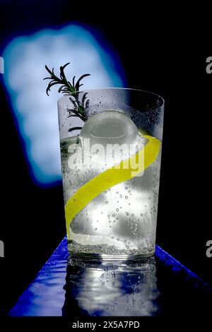 Ein erfrischendes Gin Tonic-Getränk mit Eis, einer Prise Zitronenschale und einem Zweig Rosmarin, perfekt vor blauem Hintergrund Stockfoto