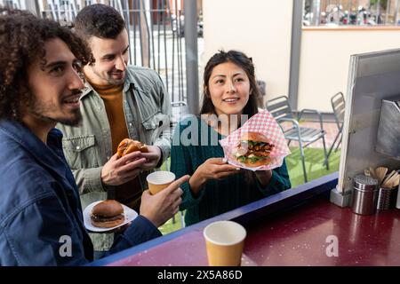 Eine vielfältige Gruppe von Freunden teilt einen Moment der Freude, während sie Gourmet Street Food aus einem Food Truck genießen und urbanen Lebensstil und Freundschaft zeigen Stockfoto