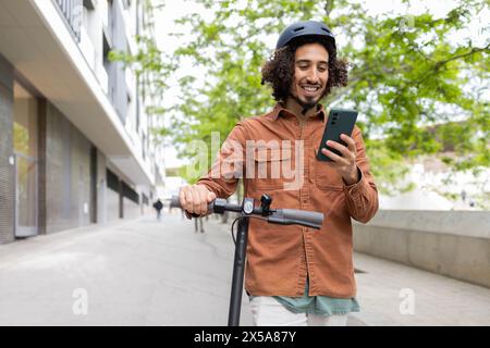 Ein lächelnder junger Erwachsener, der ein Smartphone benutzt und in einem elektrischen Roller in einer städtischen Umgebung fährt, demonstriert ein modernes, umweltfreundliches Verkehrsmittel Stockfoto