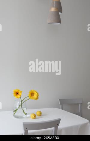 Stilleben mit Zitronen und gelben Gerberas in einem Glas auf einem Tisch, der mit Leinentischdecke bedeckt ist. Sommerkomposition mit Zitronen und gelben Blüten Stockfoto