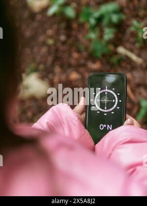 Von oben beschnittene, nicht erkennbare Mädchen genießen Sie einen gemütlichen Tag im Freien, indem Sie einen Kompass auf einem Smartphone verwenden, um durch die natürliche Umgebung zu navigieren. Stockfoto