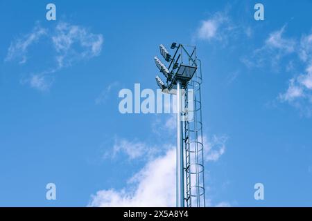 Ein hoch aufragender Zellenstandort steht vor einem ruhigen blauen Himmel, der von hellen Wolkenformationen gesäumt ist. Stockfoto