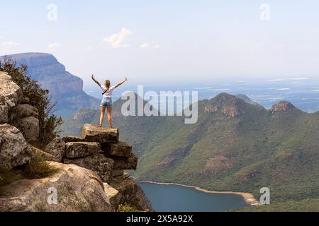 Rückansicht der nicht erkennbaren weiblichen Touristenstände mit erhobenen Armen auf einem Berg mit Blick auf den majestätischen Blyde River Canyon in Südafrika, expressi Stockfoto