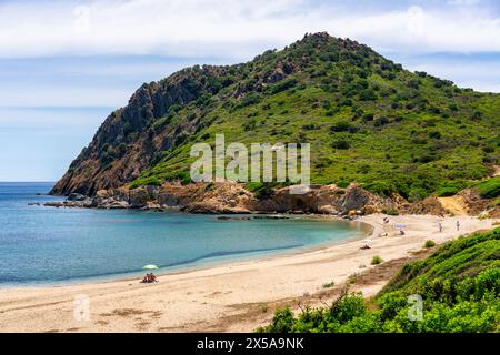 Ein ruhiger Sandstrand von Sa Figu mit ein paar Besuchern unter einem Sommerhimmel, flankiert von einem üppig grünen Berghang auf der malerischen Insel Sardinien, Ita Stockfoto