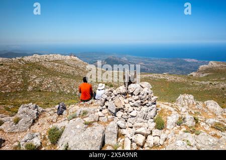 Zwei Wanderer sitzen auf einem Berg in Sardinien und bewundern die atemberaubende Aussicht auf die Küste an einem sonnigen Tag mit klarem blauem Himmel Stockfoto