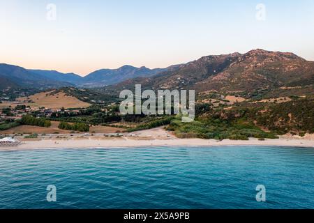Eine atemberaubende Luftaufnahme fängt den ruhigen Sonnenuntergang an der malerischen Küste Sardiniens mit sanften Hügeln und azurblauem Wasser, Porto Giunco Beach, ein Stockfoto