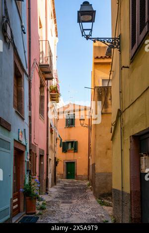 Eine enge Kopfsteinpflasterstraße, gesäumt von bunten Pastellgebäuden und traditionellen Fensterläden in Bosa Town, Sardinien, Italien, unter einem klaren blauen Himmel Stockfoto