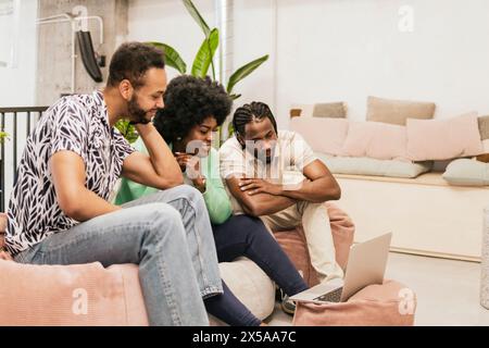 Drei Profis führen eine gemeinsame Diskussion über ein Notebook in einer hellen und eleganten Coworking-Umgebung Stockfoto